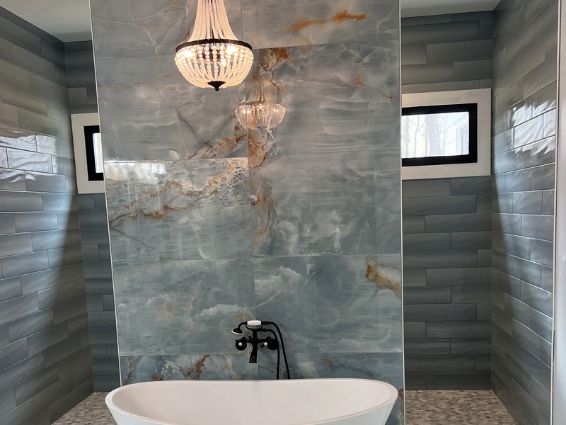 Master bath with a backlit onyx-look porcelain feature wall, a freestanding soaking tub, and a hand-beaded chandelier — a RYMAC custom build in Canton, GA.