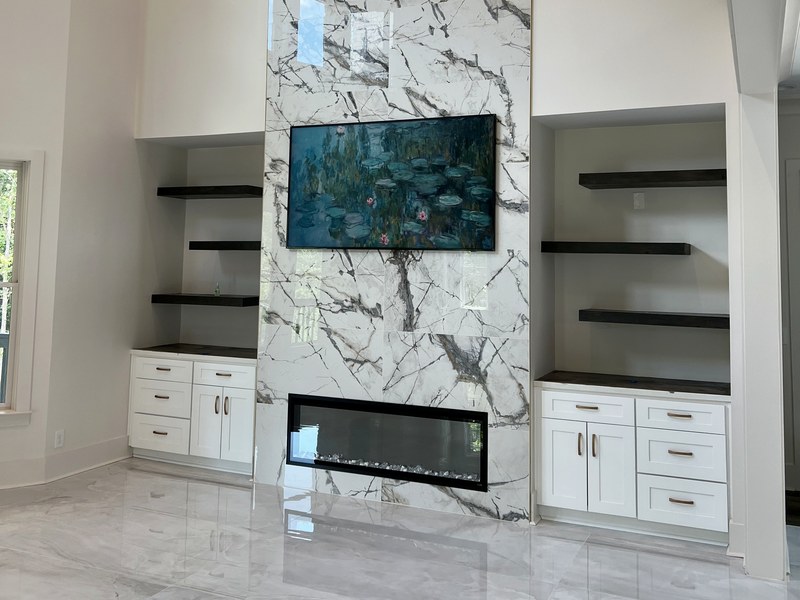 Two-story fireplace wall in large-format marble-look porcelain with custom built-ins and floating shelves — a RYMAC custom build in Suwanee, GA.