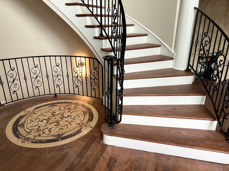 Curved staircase with custom-forged ironwork, stained-wood treads, and an inlaid wood floor medallion — a RYMAC custom home in Gainesville, GA.