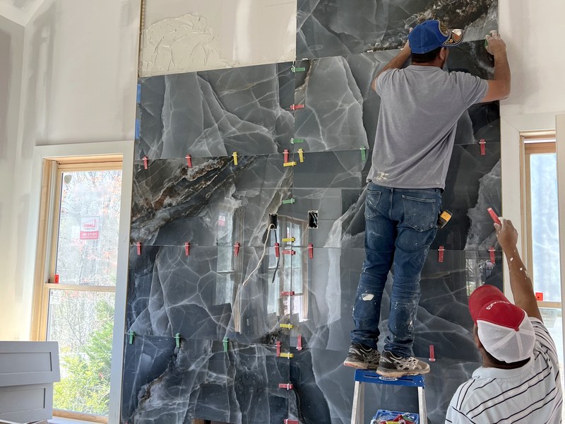 Two tile setters hand-leveling an onyx-look porcelain feature wall mid-install — a RYMAC jobsite craft shot.